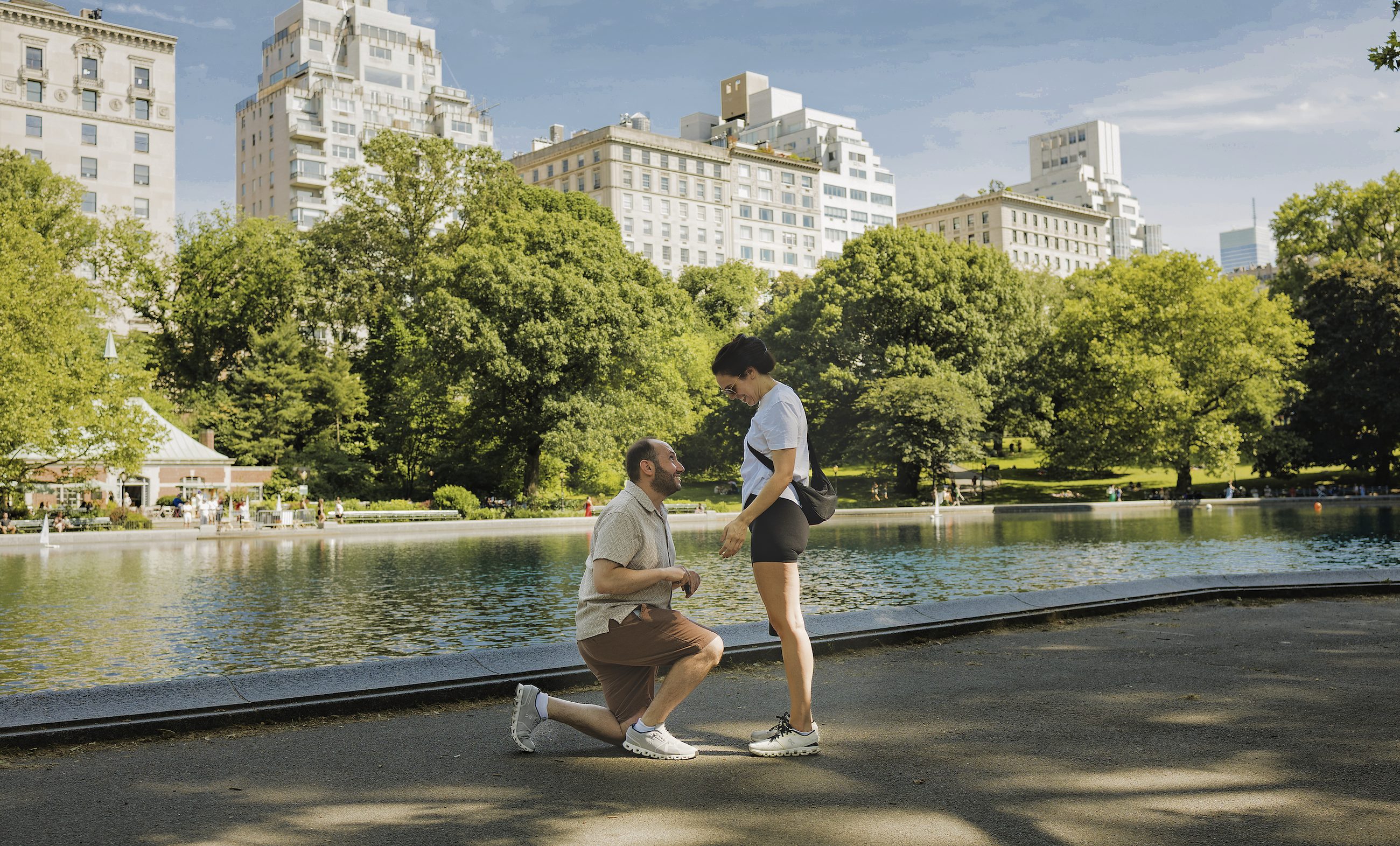 Pete kneeling to propose to Lisa beside the Conservatory Water in Central Park